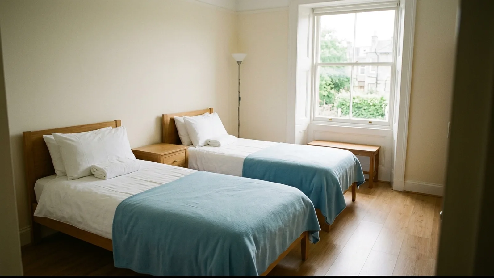 Zwei frisch bezogene Einzelbetten in einem hellen Gästezimmer, auf einem Kissen ein gefaltetes Handtuch